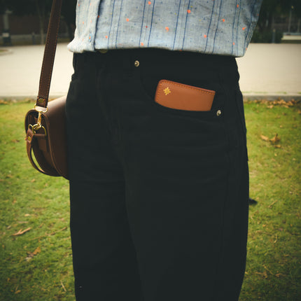 Person wearing a brown leather bag with a visible brand logo on a grassy background