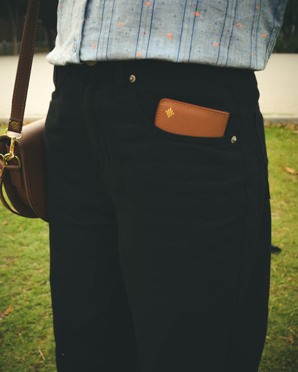Person wearing a brown leather bag with a visible brand logo on a grassy background