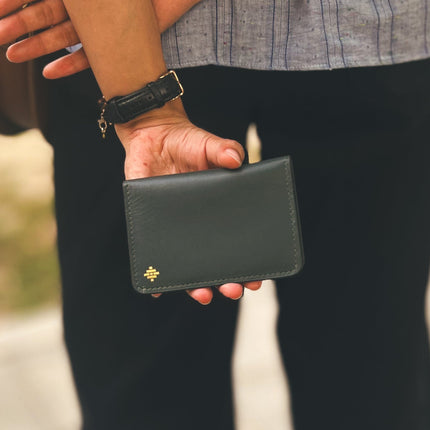 Person holding a black leather wallet with a brand logo.