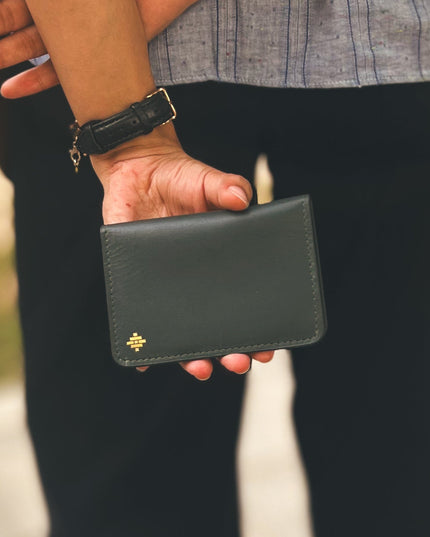 Person holding a black leather wallet with a brand logo.
